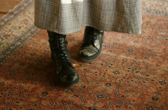 a person wearing black boots and standing on a traditional design carpet